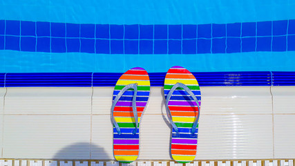 Rainbow colored flip flops at the edge of swimming pool.