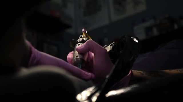 Blackwork in tattoo studio. Tattoo master makes a tattoo on a man's leg. The artist with a beard and pink gloves makes a tattoo of white paint on a black. Individuality. Be unique. White and black.