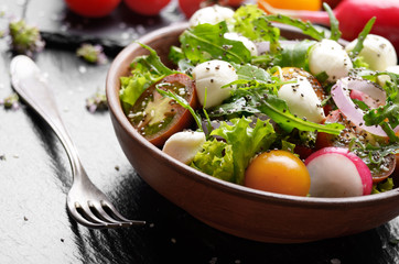 Vegetable salad with mozzarella cheese, lettuce, cherry tomatoes, radish, cucumber, onion and basil in clay dish