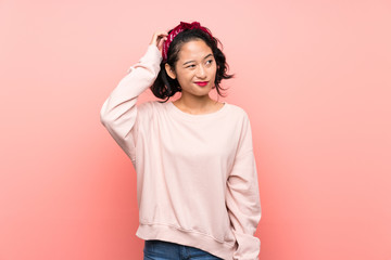 Asian young woman over isolated pink background having doubts while scratching head - obrazy, fototapety, plakaty