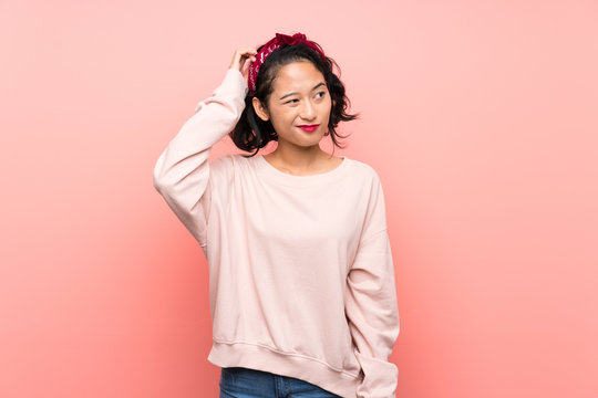 Asian young woman over isolated pink background having doubts while scratching head