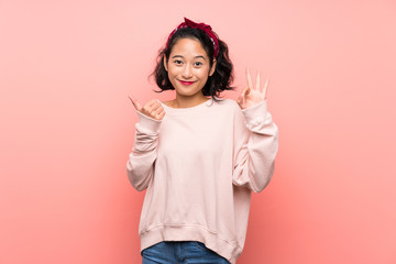 Asian young woman over isolated pink background showing ok sign and thumb up gesture