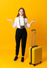 Full body of traveler teenager girl with suitcase over isolated yellow background having doubts with confuse face expression