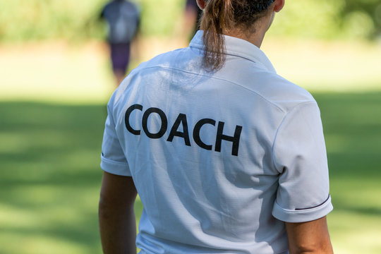 Back View Of A Female Sport Coach Watching Her Team Competing At An Outdoor Sport Field