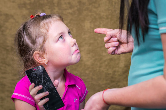 Mom punishes daughter for a broken phone. A little girl plaintively looks at parents.  The child accidentally broke the phone. The concept of children's raise