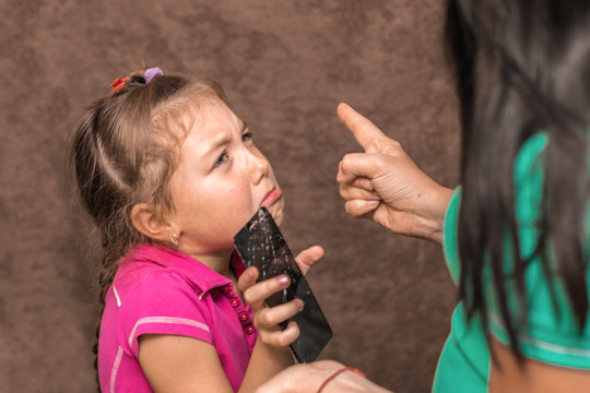 Mom scolds her daughter for a broken phone. Punishment of a child for a spoiled mobile phone. Little girl cries and apologizes. A woman holds an index finger near the face of a child.