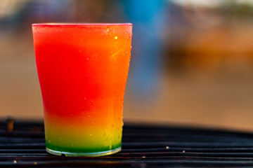 Colorful cocktail on a dark wicker table on the beach in the sunlight with some bokeh