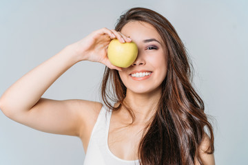 Beauty portrait of smiling young asian woman girl holding green apple near clean face on grey...