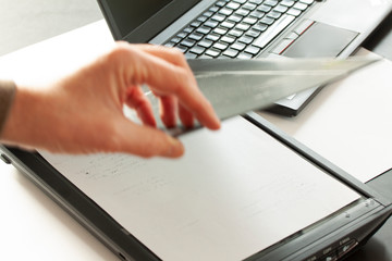 A hand puts a piece of paper closing a flatbed scanner with a laptop computer in the background. Selective focus and motion blur.