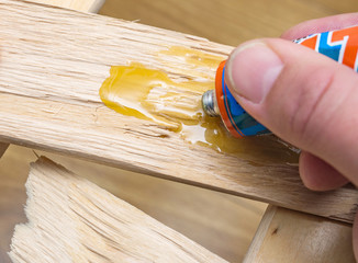 Furniture repair at home. Carpenter applies glue to a wooden cracked board. Close-up, selective...