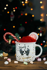 Closeup of a sleeping doll in santa claus costume. child sits in a glass with sweets. red Christmas candy. marshmallows in the foreground and wooden background