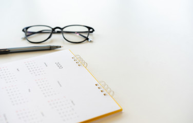 close up side view on  white calendar schedule background with pen and eyeglasses to make appointment meeting or manage timetable each day for planning work in new year 2020 resolution concept