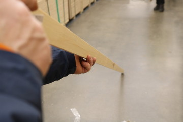 A view of a man's hand holding a long planed stick in the middle checking its evenness in the store. Shot under shop lighting.