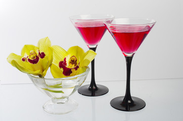 Two glasses with a cocktail and two yellow orchids in a vase.