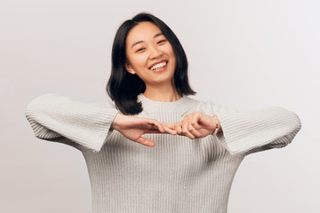 Girl stretches elbows in different directions. Laughs. Businesslike young woman Asian appearance with black hair brown eyes dressed in knitted warm sweater stands isolated white background in Studio