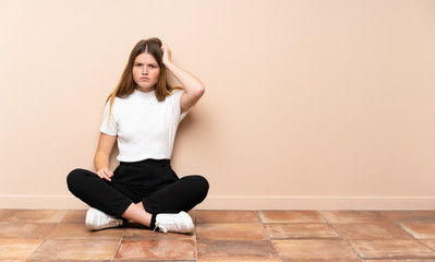 Fototapeta premium Ukrainian teenager girl sitting on the floor with an expression of frustration and not understanding