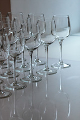 A raw of empty wine glasses on the table. Many transparent high stalk glasses on the table next to window, beautiful reflections, natural light. Catering, holiday, cafe, restaurant glassware