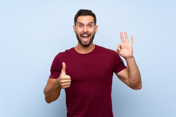 Handsome man over isolated blue background showing ok sign and thumb up gesture