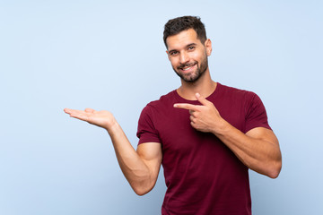 Handsome man over isolated blue background holding copyspace imaginary on the palm to insert an ad