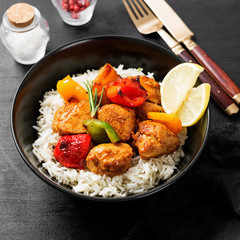 Grilled chicken breast and colorful peppers with fried rice on black background.