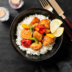 Grilled chicken breast and colorful peppers with fried rice on black background.