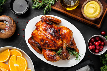 Homemade roasted chicken with oranges ,rosemary and cranberries on black wooden background.