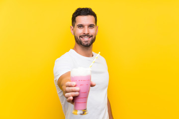 Young man with strawberry milkshake over isolated yellow background