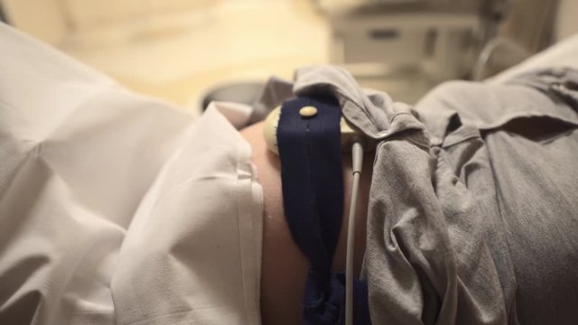 Pregnant woman in hospital with cardiotocography bell.  Ultrasonic sensors of the Fetal Monitor at the abdomen of pregnant woman.