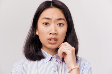 Sad concerned girl looking worried and thoughtful feeling depressed. Businesslike beautiful young woman of Asian appearance dressed in striped office shirt stands isolated white background in Studio.
