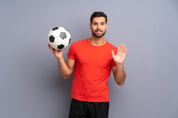 Handsome young football player man over isolated white wall saluting with hand with happy expression