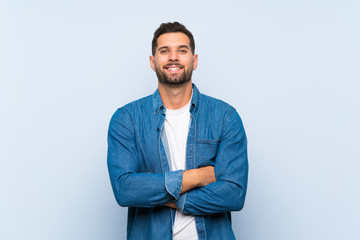 Handsome man over isolated blue background keeping the arms crossed in frontal position