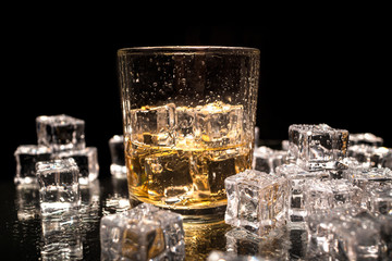 Drinking glass with drink and ice cubes, and more ice cubes on a table, with dark background