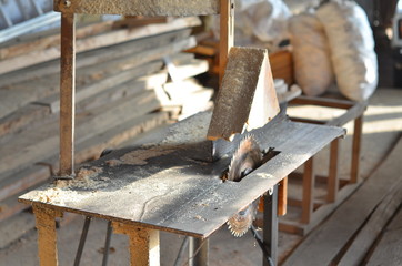 An old electrical device for sawing wooden boards stands in an old dusty workshop. In the background are composed of the old Board