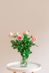 Natural pastel pink roses in a glass vase on white table on light beige background