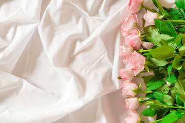 Top view of pastel pink roses on white bed background.