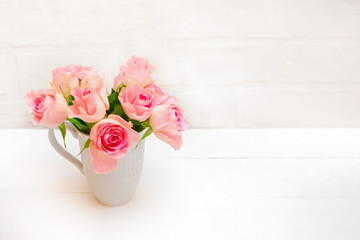 Fresh pastel pink roses in a white cup on white wooden table