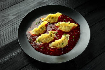 Steamed yaki Gyoza served on black plate with sweet chilli sauce and sesame seeds