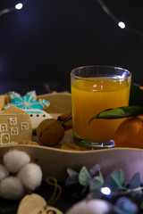 Gingerbread Christmas cookies in the shape of a house, a snowman and stars lie on a spacing with fresh orange juice in a glass of drink in a farm style. Around are nuts, cinnamon, decor. Blurred