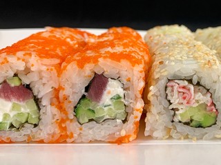 Sushi with red fish and avocado, close-up, on a black background. Japanese traditional cuisine, delicious sushi with dill and sesame seeds. Rolls - California and Philadelphia.