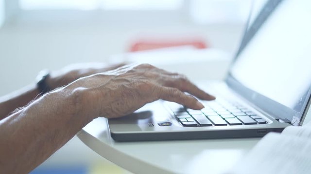 Hands of aged man typing on a laptop computer