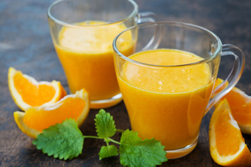 Close up two glass mugs of freshly squeezed orange juice stand on a wooden background. Horizontal orientation.