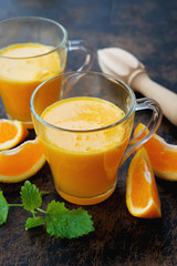 Two glass mugs of freshly squeezed orange juice stand on a wooden background. Vertical orientation.
