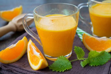Two glass mugs of freshly squeezed orange juice stand on a wooden background. Horizontal orientation.