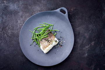 Gourmet fried Japanese skrei cod fish filet with glasswort and furikake as top view on a modern...