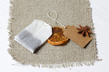 A bag of tea, anise and slices of dried tangerines. Lying on a piece of linen. Against the background of white painted boards.