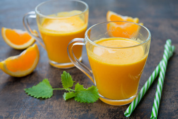 Two glass mugs of freshly squeezed orange juice stand on a wooden background. Horizontal orientation.