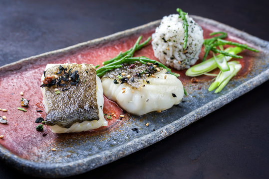 Gourmet Fried Japanese Skrei Cod Fish Filet With Glasswort And Furikake Onigiri As Closeup On A Modern Design Plate