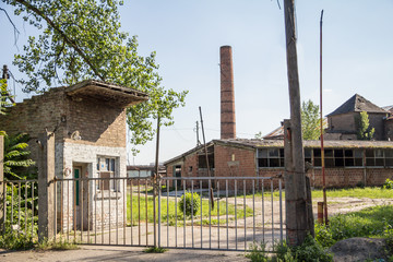 Fototapeta na wymiar Entrance to an Abandoned factory and warehouse with its distinctive brick chimnet in Eastern Europe, in Pancevo, Serbia, former Yugoslavia, during a sunny afternoon