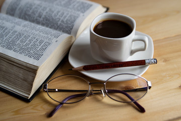 Good morning! A Cup of coffee on a warm background. The open Bible. Glasses.