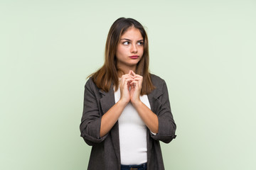 Young brunette girl with blazer over isolated green background scheming something